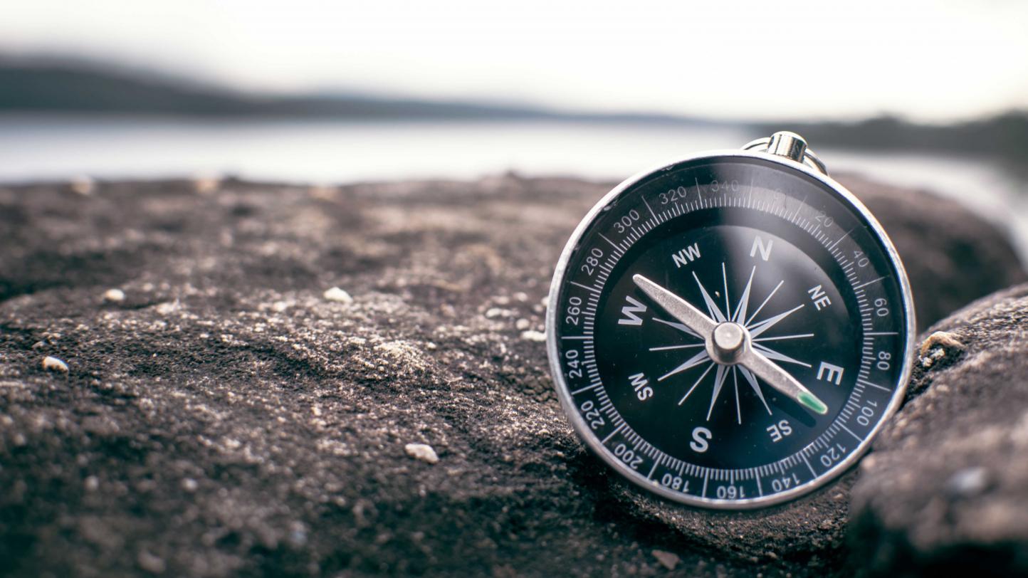 Image of a compass on rocks by the shore.