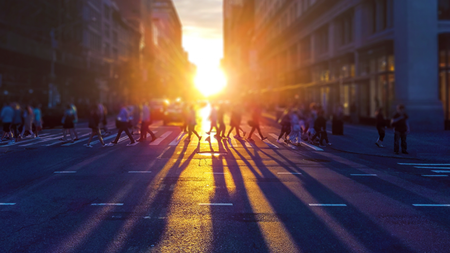 People using a crosswalk at sunset.