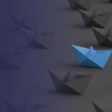 Blue paper boat among black paper boats